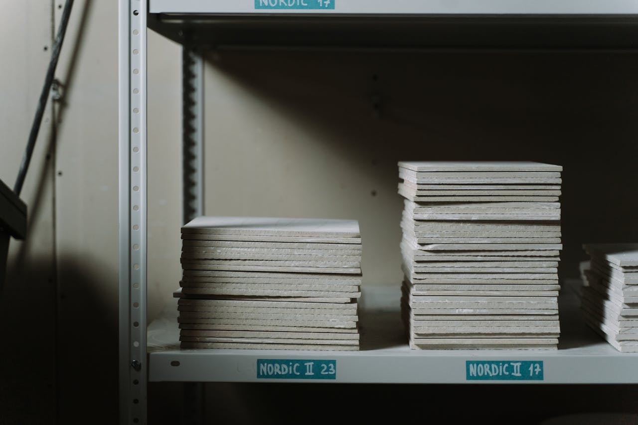 O nama Stacks of ceramic tiles neatly arranged on industrial shelves in a dimly lit warehouse.